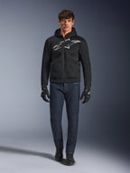 Motorrijder die de Alpinestars Chrome Superairflow Hoodie in zwart en grijs draagt, gecombineerd met een donkerblauwe jeans, zwarte motorhandschoenen en zwarte schoenen. De hoodie is voorzien van een groot gestileerd logo op de borst en een 3D mesh-textuur voor prestaties bij hoge temperaturen.