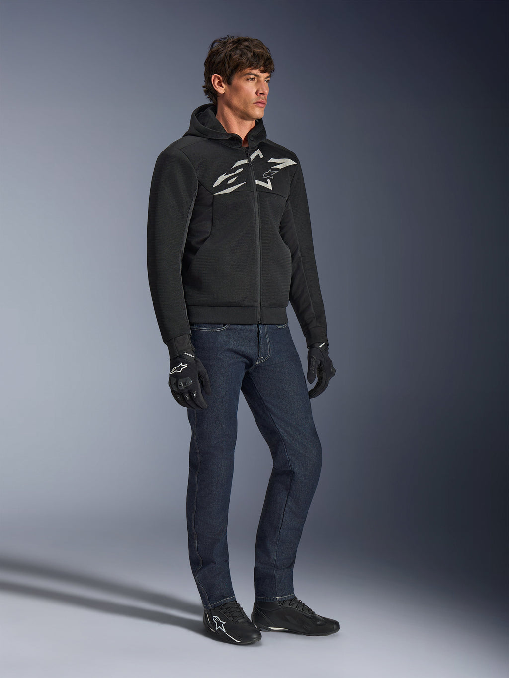 Alpinestars Chrome Superairflow Hoodie, zwart met wit en grijs logo, 3D-mesh geventileerde textielconstructie, gedragen met donkerblauwe denim jeans en zwarte motorhandschoenen, urban sportieve rijstijl