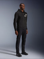Alpinestars Chrome V2 Sport Hoodie, zwarte motorhoodie met wit sterlogo, gedragen door een mannelijk model met bijpassende zwarte broek en motorsneakers, urban lifestyle motorkleding