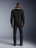 Alpinestars Chrome V2 Sport Hoodie, motorhoodie, zwart, achteraanzicht van model die een zwarte tech fleece hoodie draagt met wit Alpinestars-logo op de capuchon, gecombineerd met zwarte broek en laarzen, casual urban rijstijl
