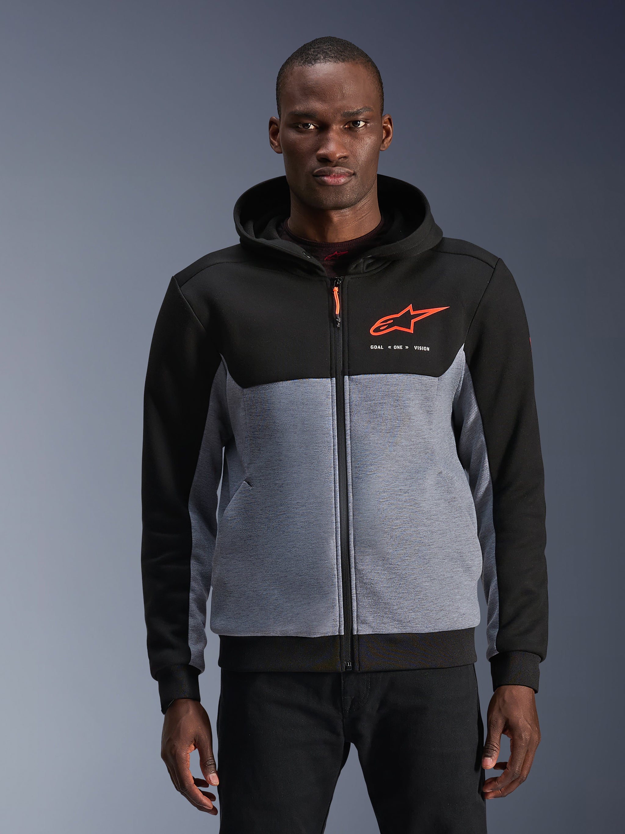 Alpinestars Chrome V2 Sport Hoodie, urban motorhoodie, zwart en grijs gemêleerd met Red Fluo accenten, voorzien van het Alpinestars-logo en "GOAL ONE VISION" tekst, casual beschermende kleding voor stadsgebruik, gedragen door een model tegen een grijze achtergrond.
