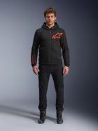 Alpinestars Chrome Air Sport Hoodie, zwart en fluorrood, urban motorhoodie met tech fleece constructie, voorzien van een groot rood Astars-logo op de borst en merknaam op de mouw, gedragen door een model met een zwarte broek en motorschoenen