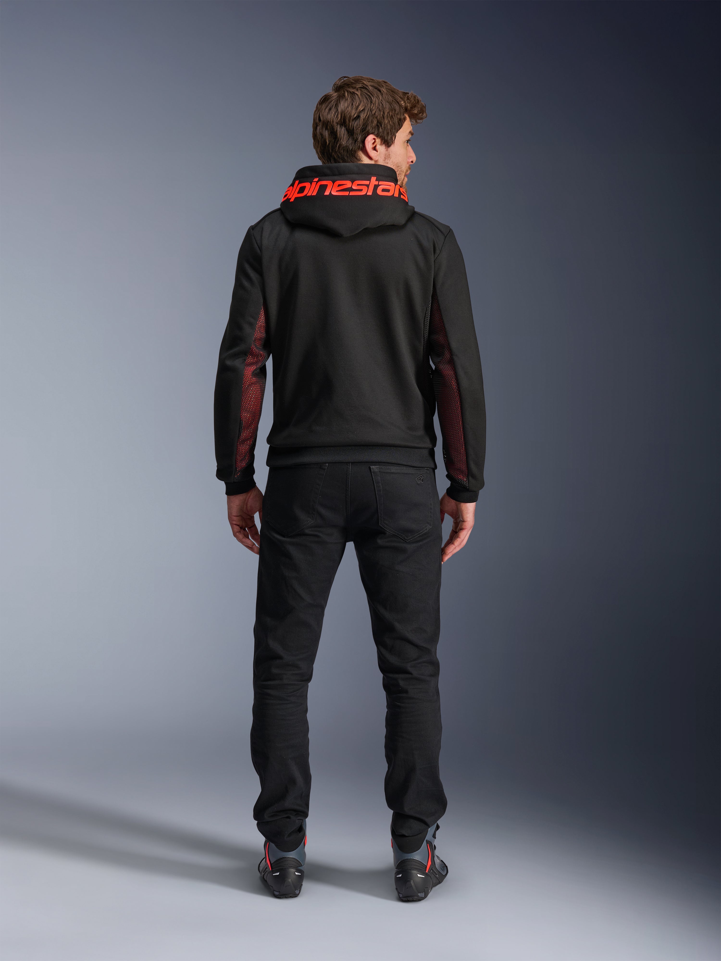 Alpinestars Chrome Air Sport Hoodie, casual motorjas, zwart en fluorood, achteraanzicht van een man die de hoodie draagt, met rode Alpinestars-branding op de capuchon en rode mesh-panelen op de mouwen, gecombineerd met een zwarte broek.