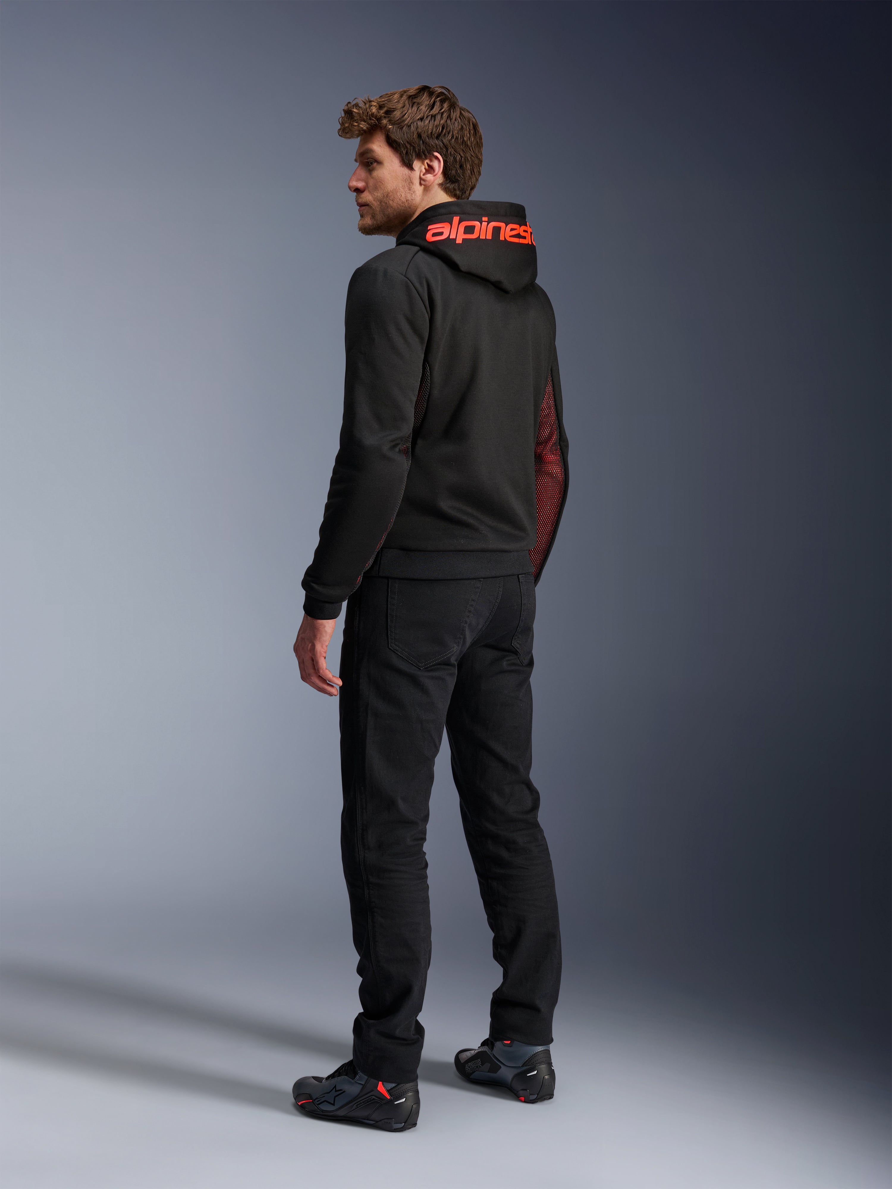 Alpinestars Chrome Air Sport Hoodie, urban motorhoodie, zwart en fluo rood, achteraanzicht met rode Alpinestars-branding op de capuchon en mesh zijpanelen, gedragen met zwarte motorbroek en technisch schoeisel