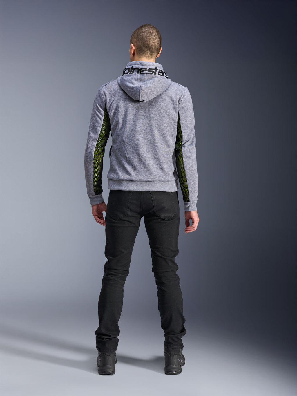 Alpinestars Chrome Air Sport Hoodie, Gray Heather Black, achteraanzicht van een motorhoodie met groene high-flow mesh panelen aan de zijkanten en mouwen, tech fleece-constructie met Alpinestars-branding op de capuchon, gedragen met een zwarte broek