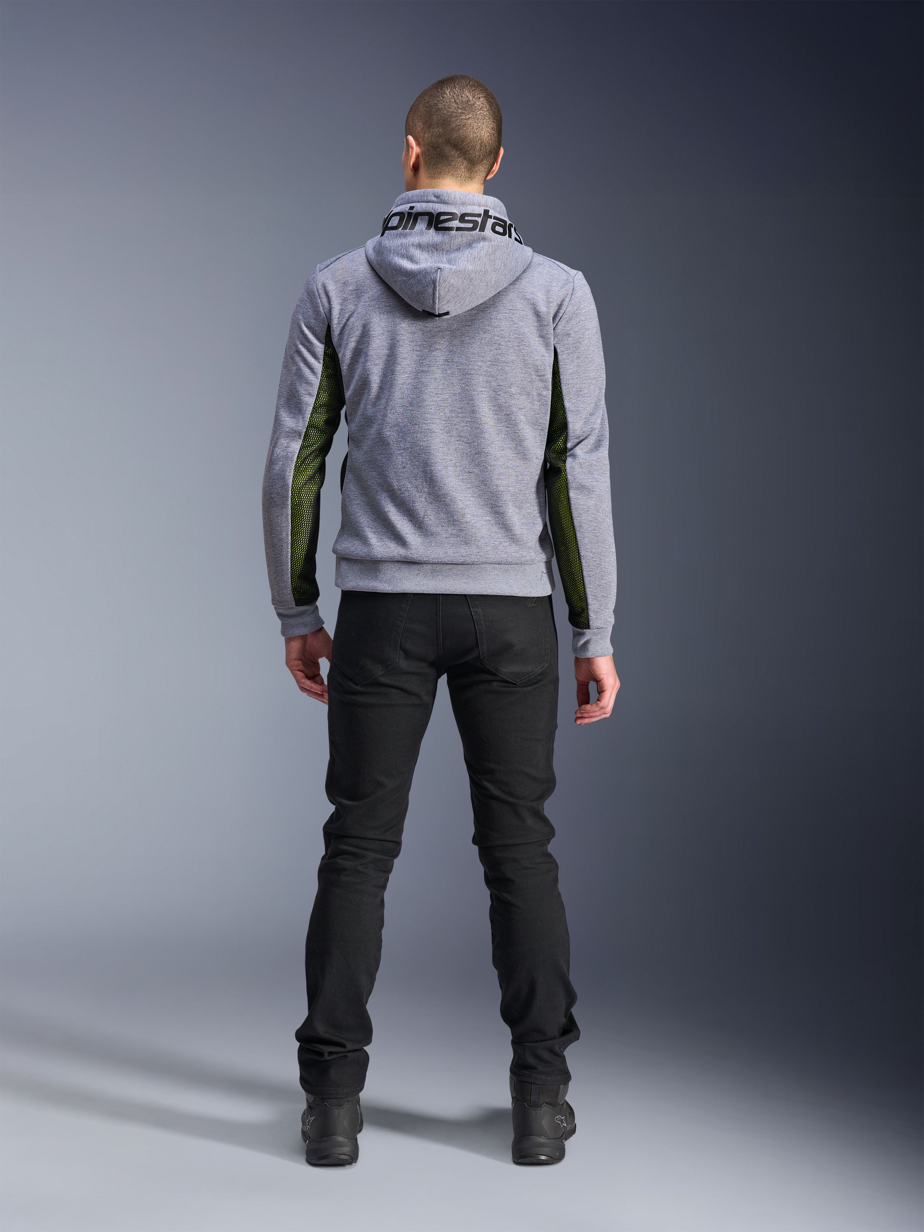 Alpinestars Chrome Air Sport Hoodie, Gray Heather Black, achteraanzicht van een motorhoodie met groene high-flow mesh panelen aan de zijkanten en mouwen, tech fleece-constructie met Alpinestars-branding op de capuchon, gedragen met een zwarte broek
