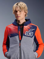 Alpinestars MM93 Chrome V2 Sport Hoodie, stedelijke motorhoodie, Blue Navy en Gray Mel met Red Fluo accenten, voorzien van Marc Marquez 93-branding en Alpinestars-logo, ontwerp met volledige ritssluiting, casual lifestyle kleding voor motorrijders, model draagt de hoodie