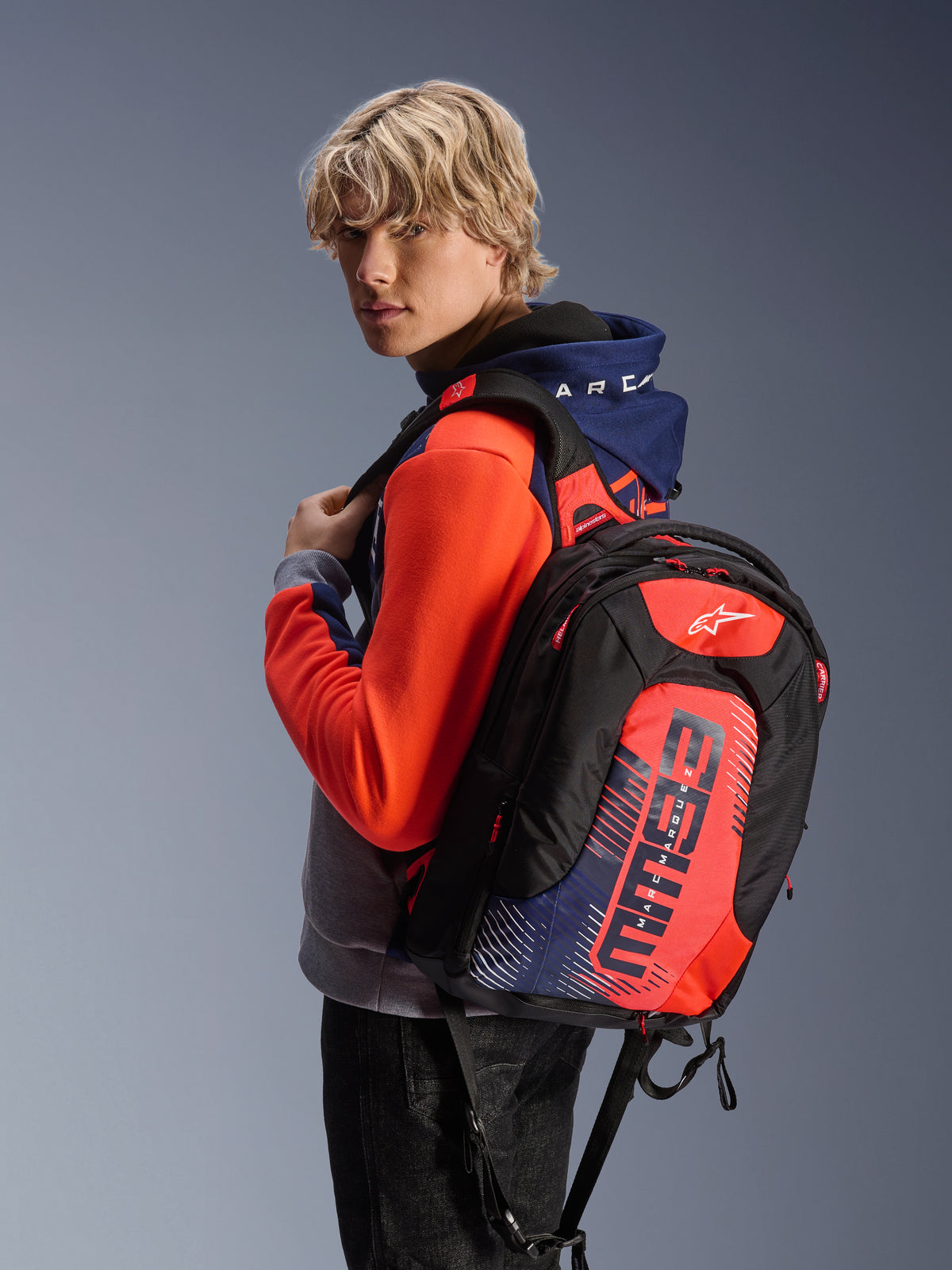 Alpinestars MM93 City Hunter V2 rugzak, zwart met fluorood en marineblauwe accenten, met Marc Marquez MM93 signature graphics, gedragen met een bijpassende sport hoodie, gestroomlijnd aerodynamisch profiel voor motorrijders