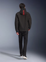 Alpinestars Radium Tech Hoodie, urban motorcycle jacket, Black, back view featuring bright red 'ALPINE' text on the hood, worn with black pants and sneakers, sleek technical shell for commuting.