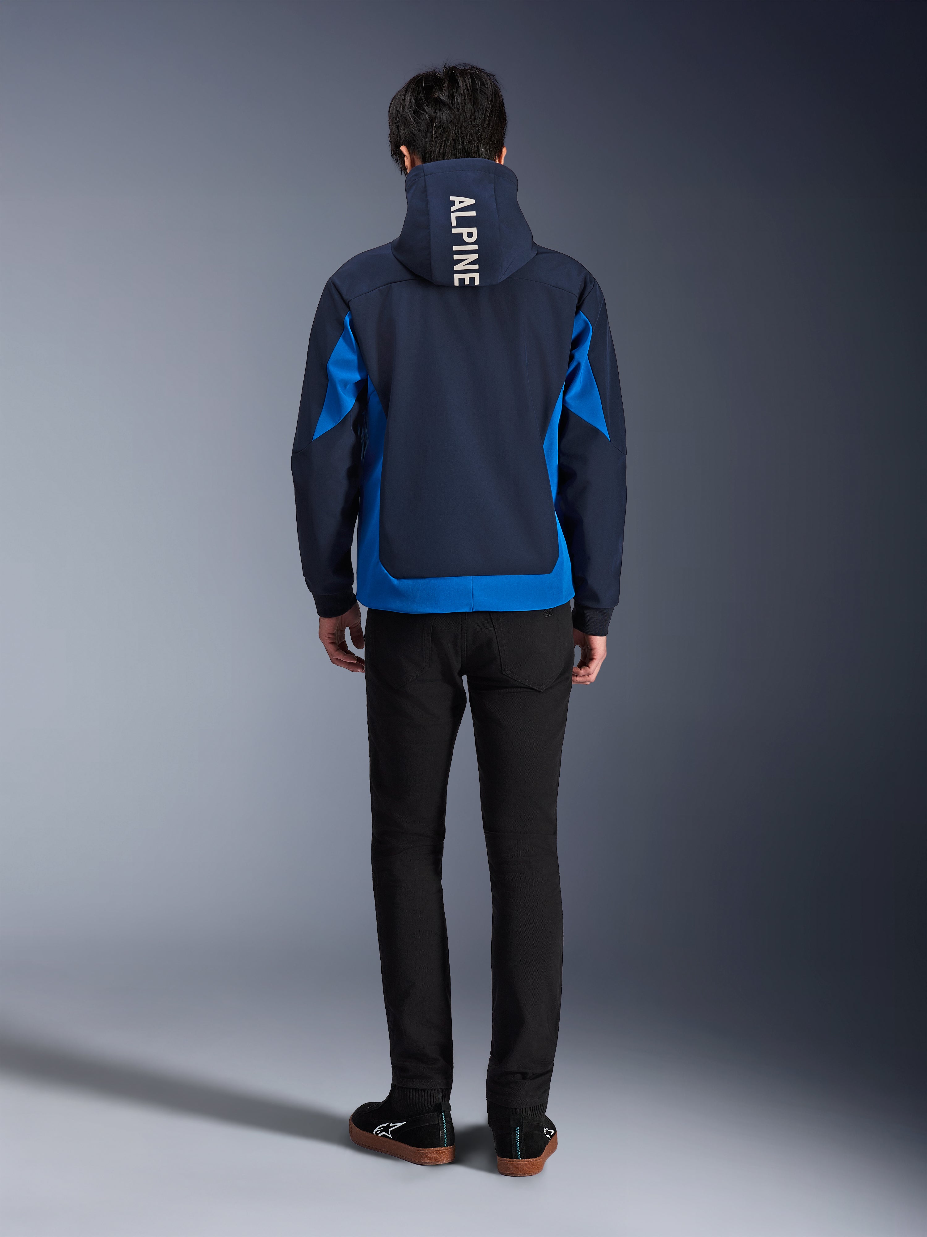 Alpinestars Radium Tech Hoodie, Night Navy en Royal Blue, achteraanzicht met verticale 'ALPINE' branding op de capuchon, royal blue zijpanelen en zoom, casual stedelijke motorhoodie met winddichte 3L shell, gedragen met zwarte broek