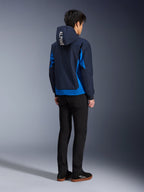 Alpinestars Radium Tech Hoodie, Night Navy en Royal Blue, achteraanzicht van model in de technische shell hoodie met witte 'ALPINE' tekst op de capuchon, gecombineerd met een zwarte broek en schoenen, stedelijke motoruitrusting