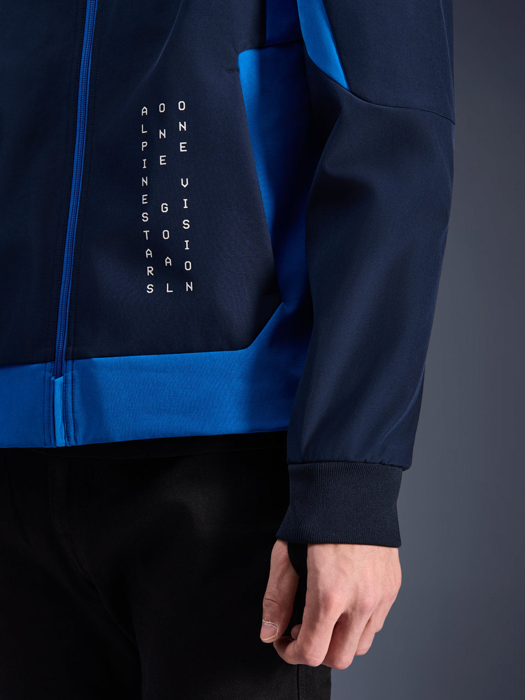 Alpinestars Radium Tech Hoodie, stedelijke motorhoodie, Night Navy en Royal Blue, close-up detail van het zijpaneel met witte verticale tekstafbeelding, geribde stretch manchet en blauwe ritssluiting