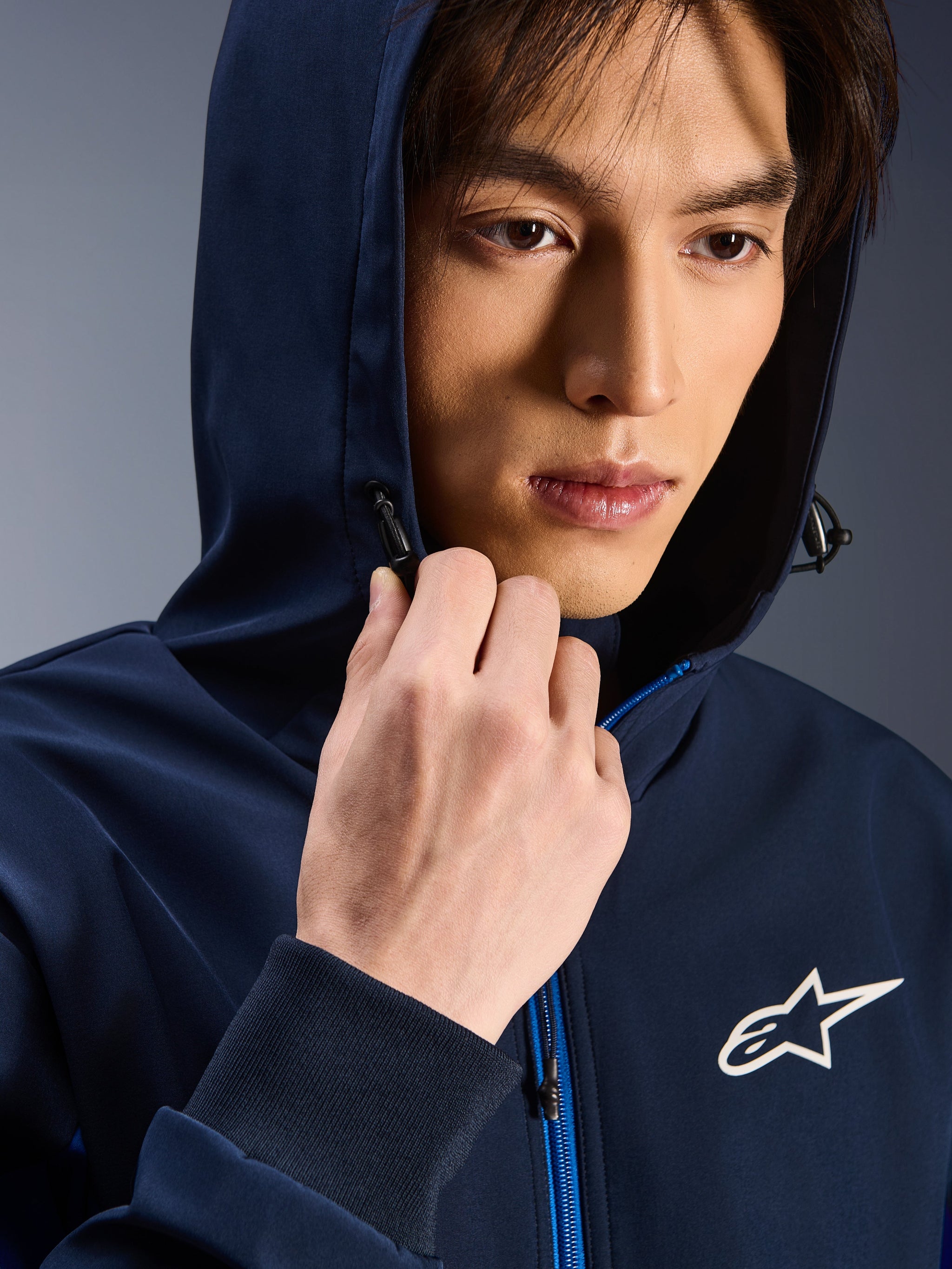 Alpinestars Radium Tech Hoodie, Night Navy Royal Blue, close-up of man wearing the hoodie with hood up, white Astars logo on chest, blue zipper, urban technical riding shell
