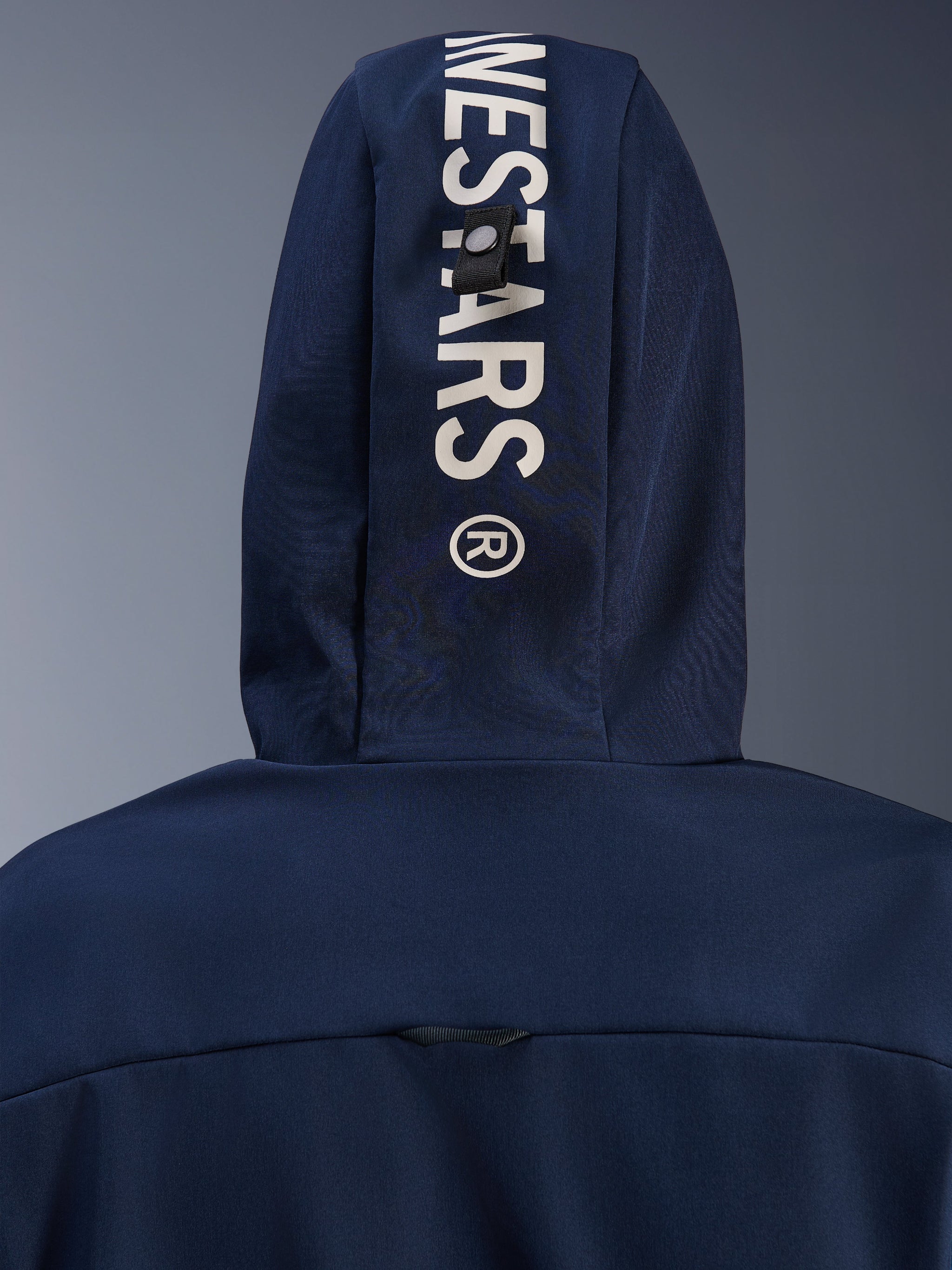 Alpinestars Radium Tech Hoodie in Night Navy Royal Blue, close-up of the back hood featuring vertical white Alpinestars branding and a secure loop attachment system, urban motorcycle technical apparel.