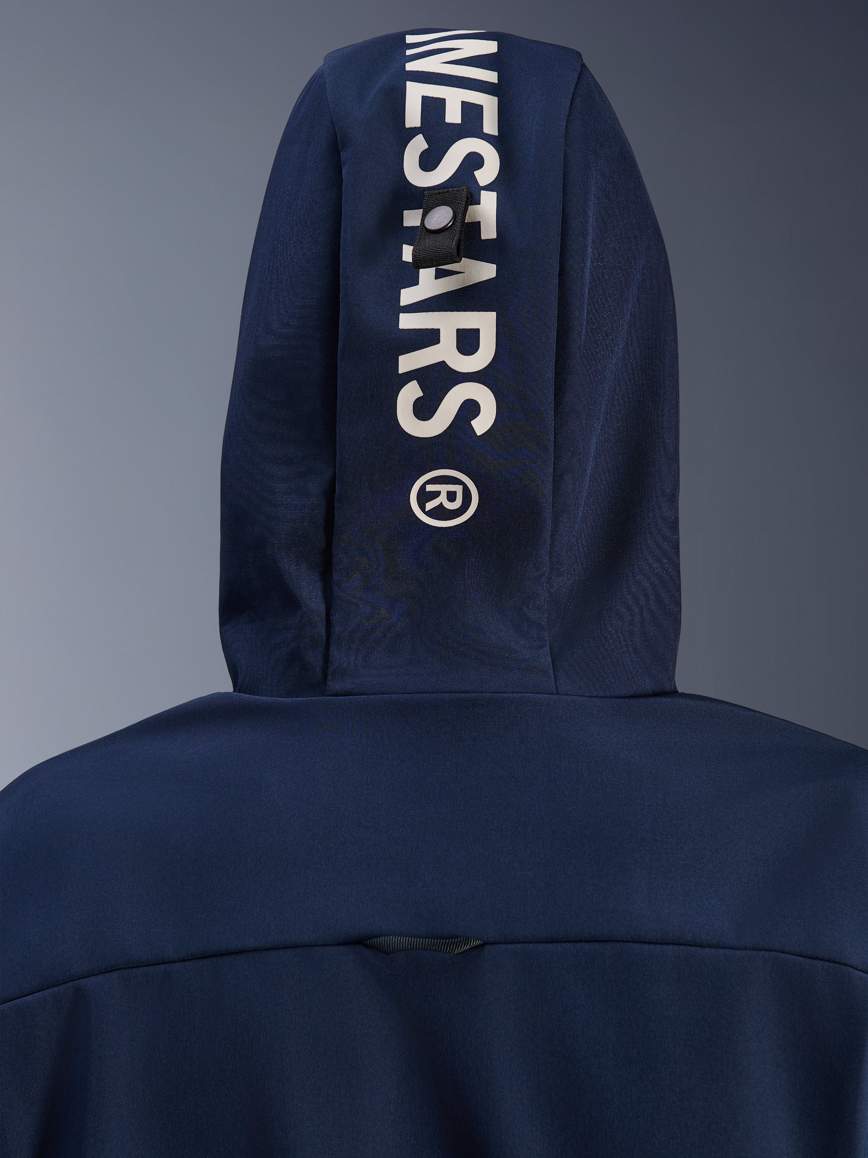 Alpinestars Radium Tech Hoodie in Night Navy Royal Blue, close-up van de capuchon aan de achterzijde met verticale witte Alpinestars-branding en een veilig lusbevestigingssysteem, technische stedelijke motorkleding.