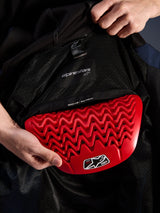 Alpinestars Radium Tech Hoodie interior detail, red Nucleon Plasma back protector being inserted into the back protector pocket, black mesh lining with 'READY FOR | Back Protector' text, wavy honeycomb armor design, technical urban motorcycle jacket protection features