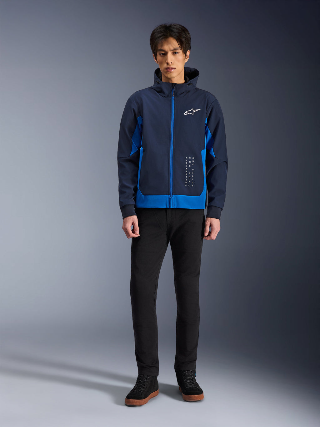Alpinestars Radium Tech Hoodie, Night Navy en Royal Blue stedelijke motorhoodie, winddichte technische shell, casual streetwear-ontwerp gedragen met zwarte broek en hoge sneakers, voorzien van wit logo op de borst.