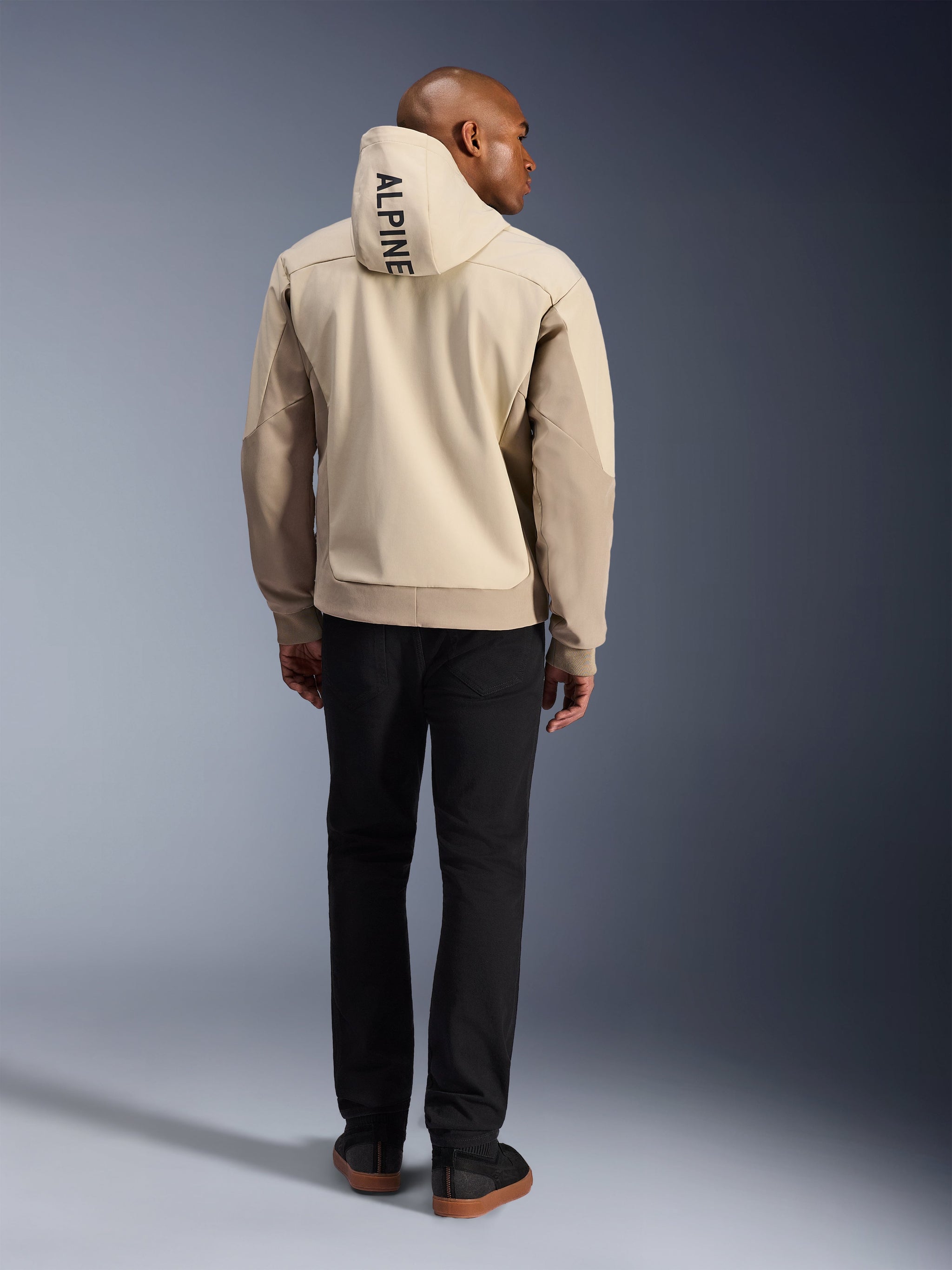 Alpinestars Radium Tech Hoodie, Mastic Aluminum, achteraanzicht met verticale 'ALPINE' tekst op de capuchon, technische 3L winddichte shell urban motorjas met beige panelen, gedragen met zwarte broek