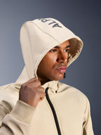 Alpinestars Radium Tech Hoodie in Mastic Aluminum, close-up van een man met de capuchon op, voorzien van Alpinestars-branding op de bovenkant, stedelijke motorjas met technische winddichte shell, moderne streetwear-esthetiek voor stadsritten