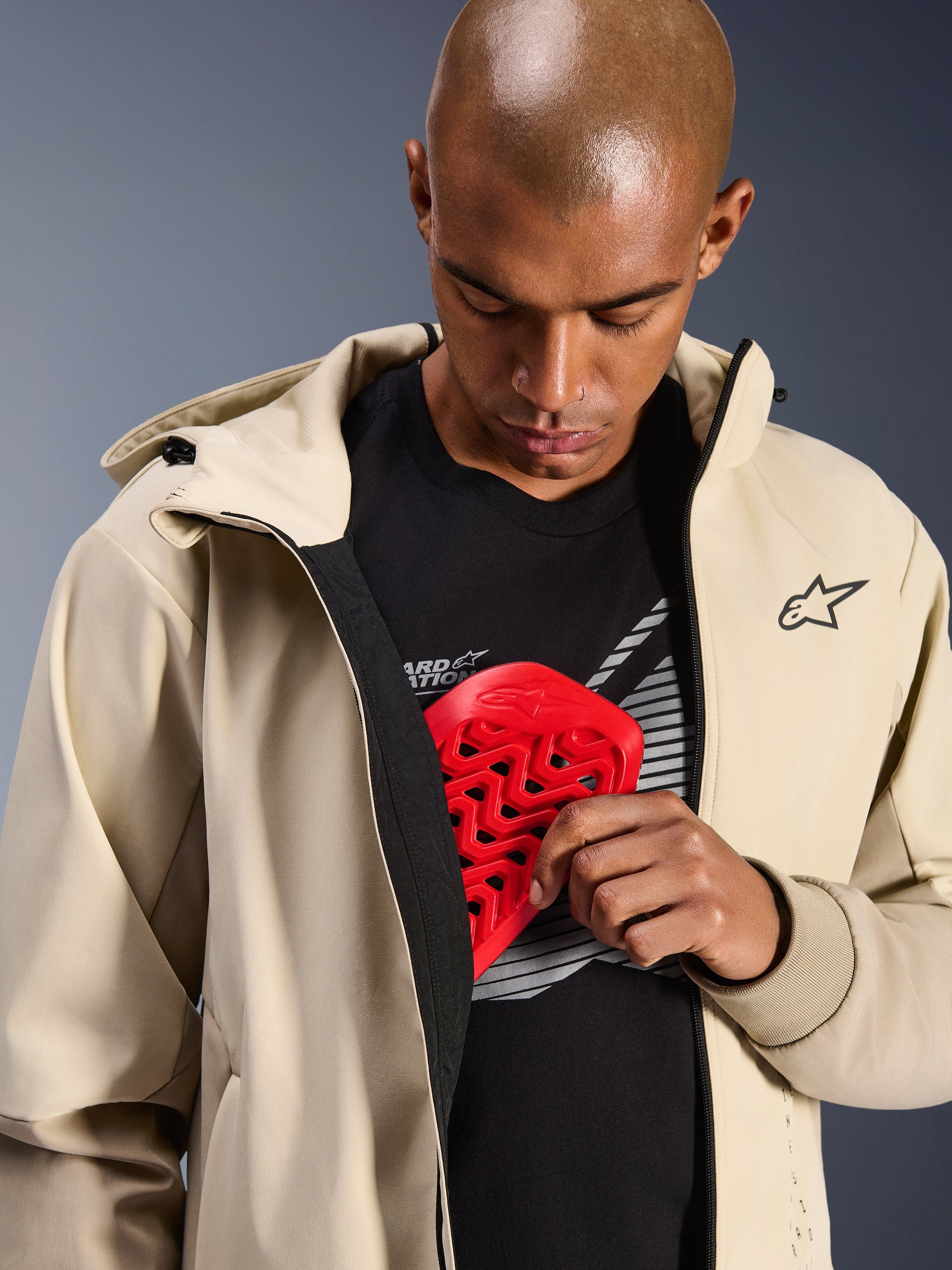 Alpinestars Radium Tech Hoodie in Mastic Aluminum, stedelijke motorjas, model toont de interne zak voor protectie met een rode Nucleon borstbeschermer, winddichte tech-shell met een casual hoodie-ontwerp en Alpinestars-branding.