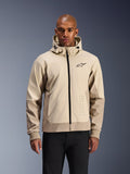 Alpinestars Radium Tech Hoodie in Mastic Aluminum, lichtbeige en tan stedelijke motorjas, zwarte rits aan de voorzijde en klein borstlogo, gedragen door een man in een zwarte broek, technische winddichte shell met eigentijdse streetwear-stijl