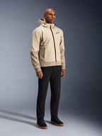 Alpinestars Radium Tech Hoodie, urban motorjas, Mastic Aluminum lichtbeige, gedragen met zwarte broek en zwarte hoge sneakers, voorzien van een technische winddichte buitenlaag, ritssluiting aan de voorzijde en afneembare capuchon, modern streetwear-design voor stedelijk rijden