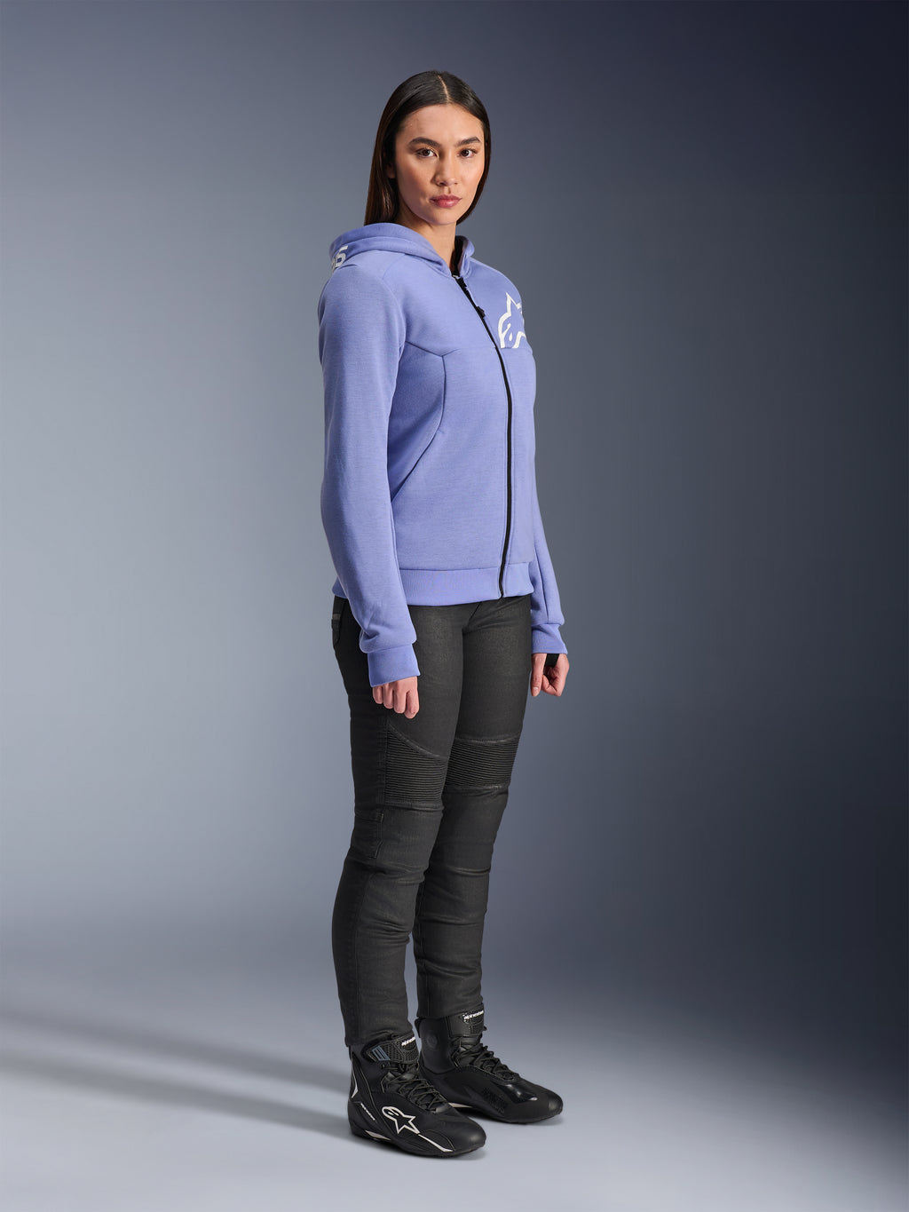 Alpinestars Stella Chrome V2 Sport Hoodie voor dames, motorhoodie in blauw-violet met wit Alpinestars-logo op de borst, model draagt zwarte motorbroek en zwarte motorlaarzen, stedelijke motorkleding voor dames
