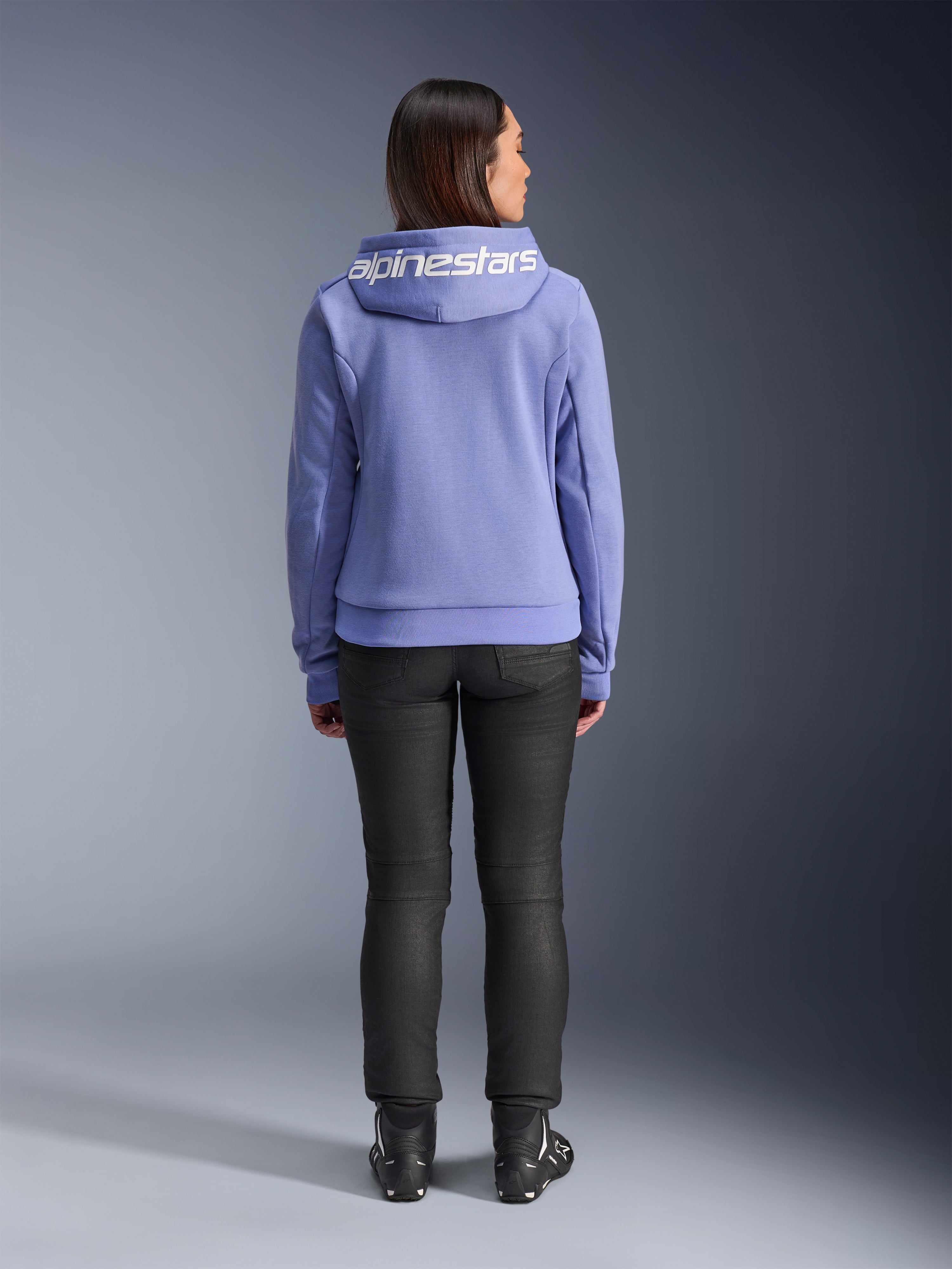 Alpinestars Stella Chrome V2 Sport Hoodie, Blue Violet, achteraanzicht van een vrouw die de hoodie draagt met wit Alpinestars-logo op de capuchon, gecombineerd met zwarte broek en motorlaarzen, casual stedelijke motorkleding