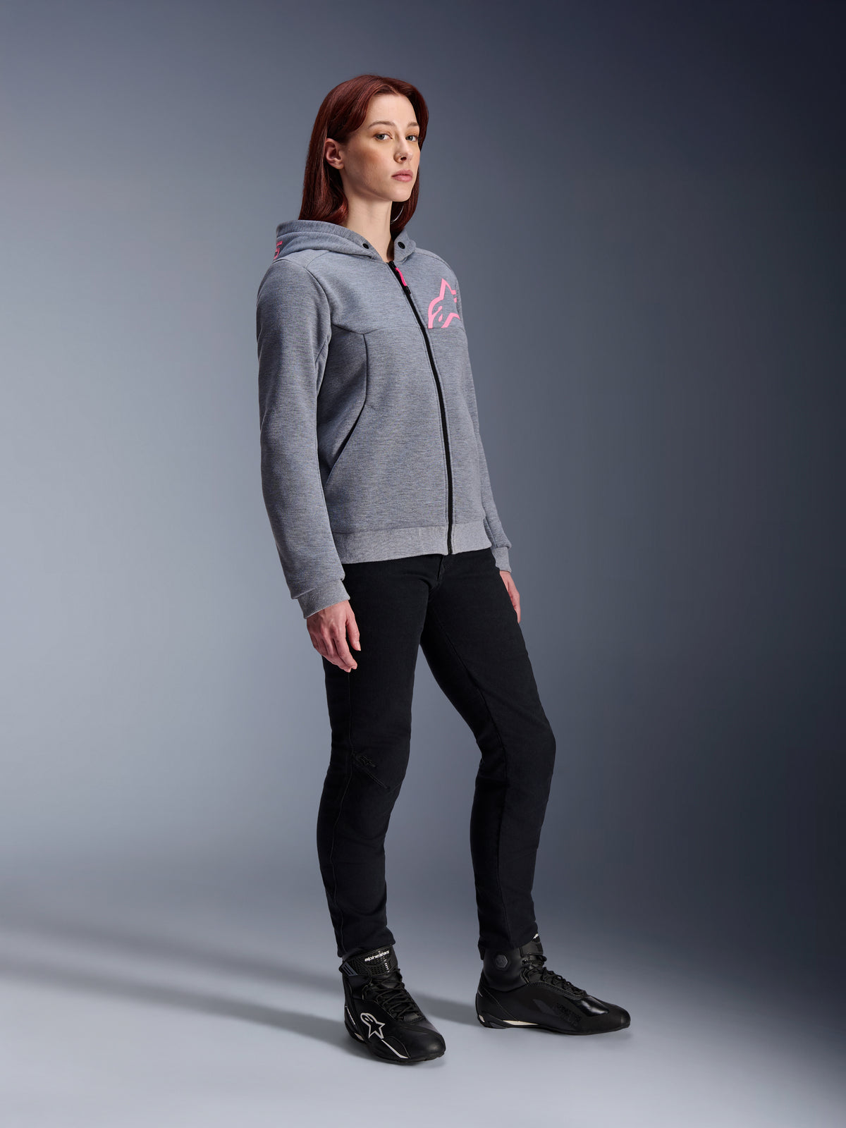 Alpinestars Stella Chrome V2 Sport Hoodie, motorhoodie voor dames, gemêleerd grijs en fluoroze, gedragen met een zwarte motorbroek en zwarte laarzen, casual urban motorkleding