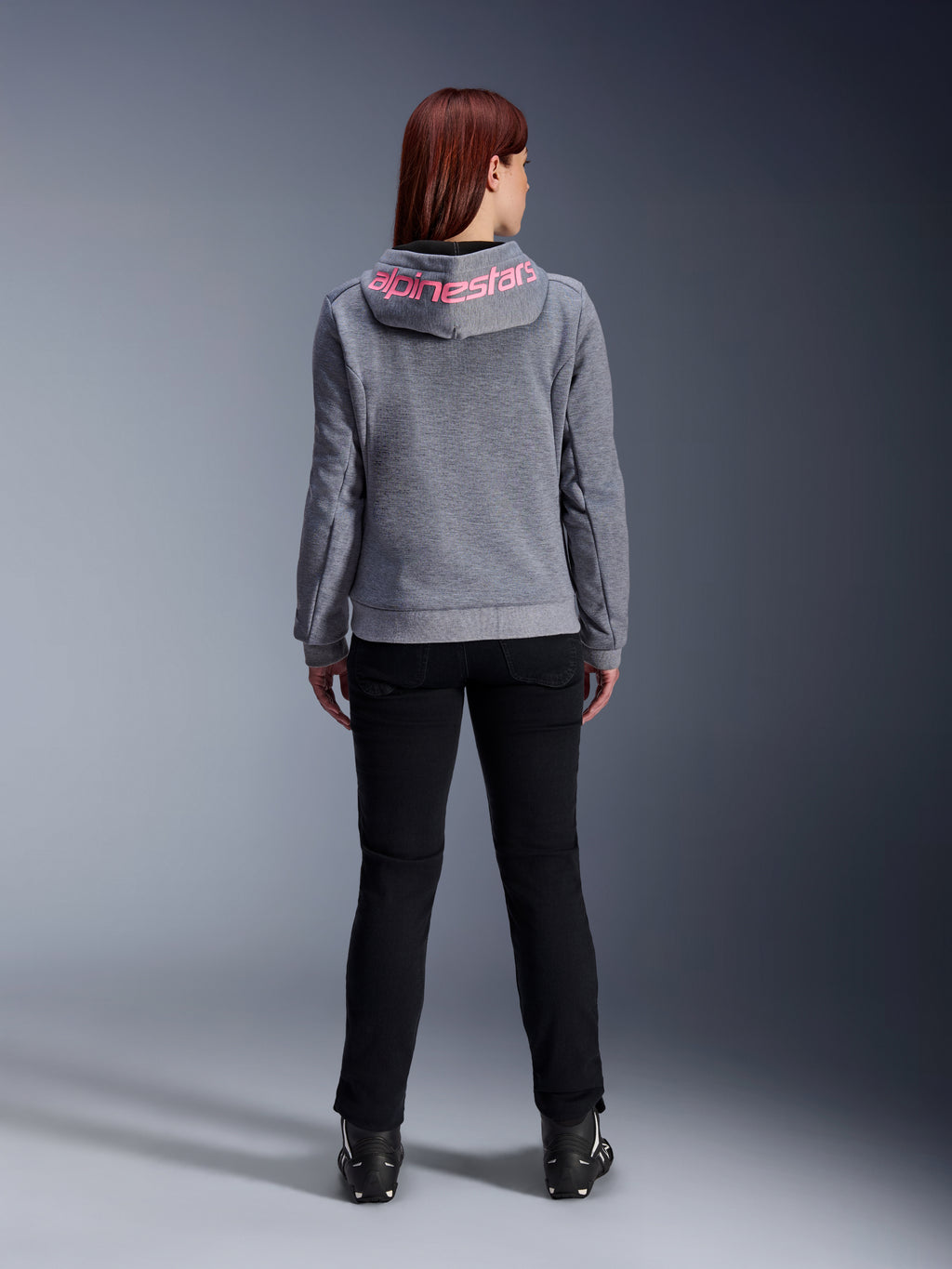 Alpinestars Stella Chrome V2 Sport Hoodie, motorhoodie voor dames, Gray Heather en Pink Fluo, achteraanzicht met roze Alpinestars-logo op de capuchon, gedragen met een zwarte motorbroek en laarzen, casual motorkleding voor dames