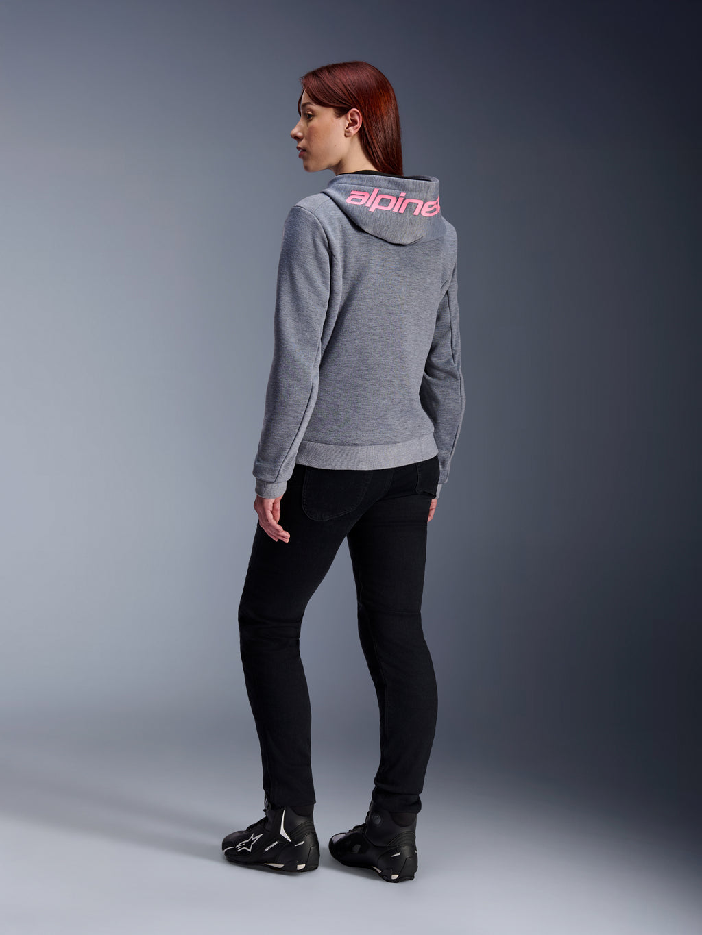 Alpinestars Stella Chrome V2 Sport Hoodie, motorhoodie voor dames, grijs gemêleerd met Pink Fluo branding op de capuchon, achteraanzicht, gedragen met zwarte broek en motorschoenen, casual stedelijke streetstyle met motorbescherming