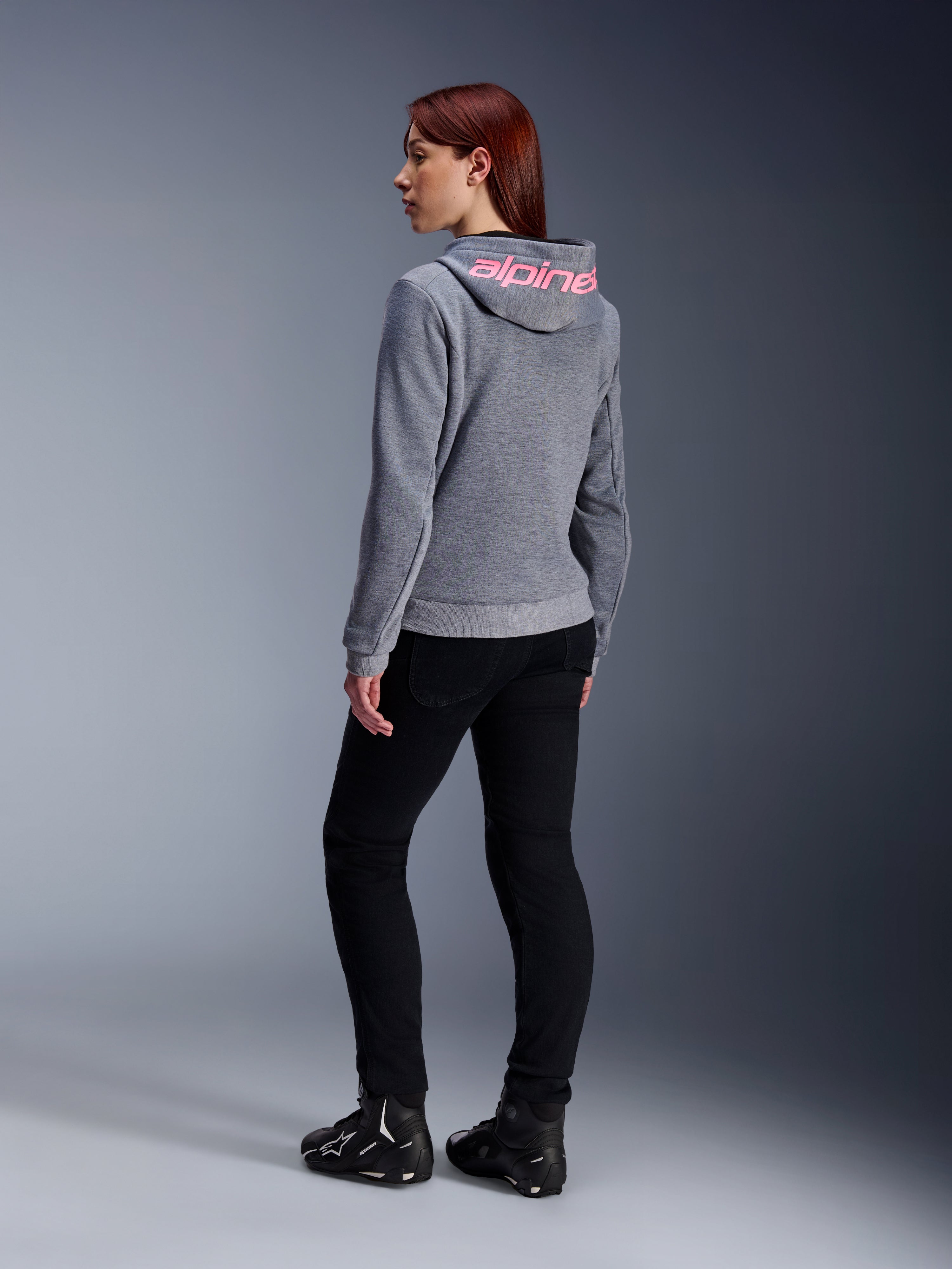 Alpinestars Stella Chrome V2 Sport Hoodie, motorhoodie voor dames, grijs gemêleerd met Pink Fluo branding op de capuchon, achteraanzicht, gedragen met zwarte broek en motorschoenen, casual stedelijke streetstyle met motorbescherming