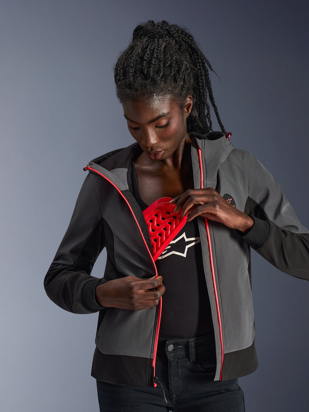 Alpinestars Stella Radium Tech Hoodie voor dames in Deep Gray en zwart, model toont de uitneembare rode Nucleon Flex Plus protectie, urban motorhoodie met roze ritsaccenten