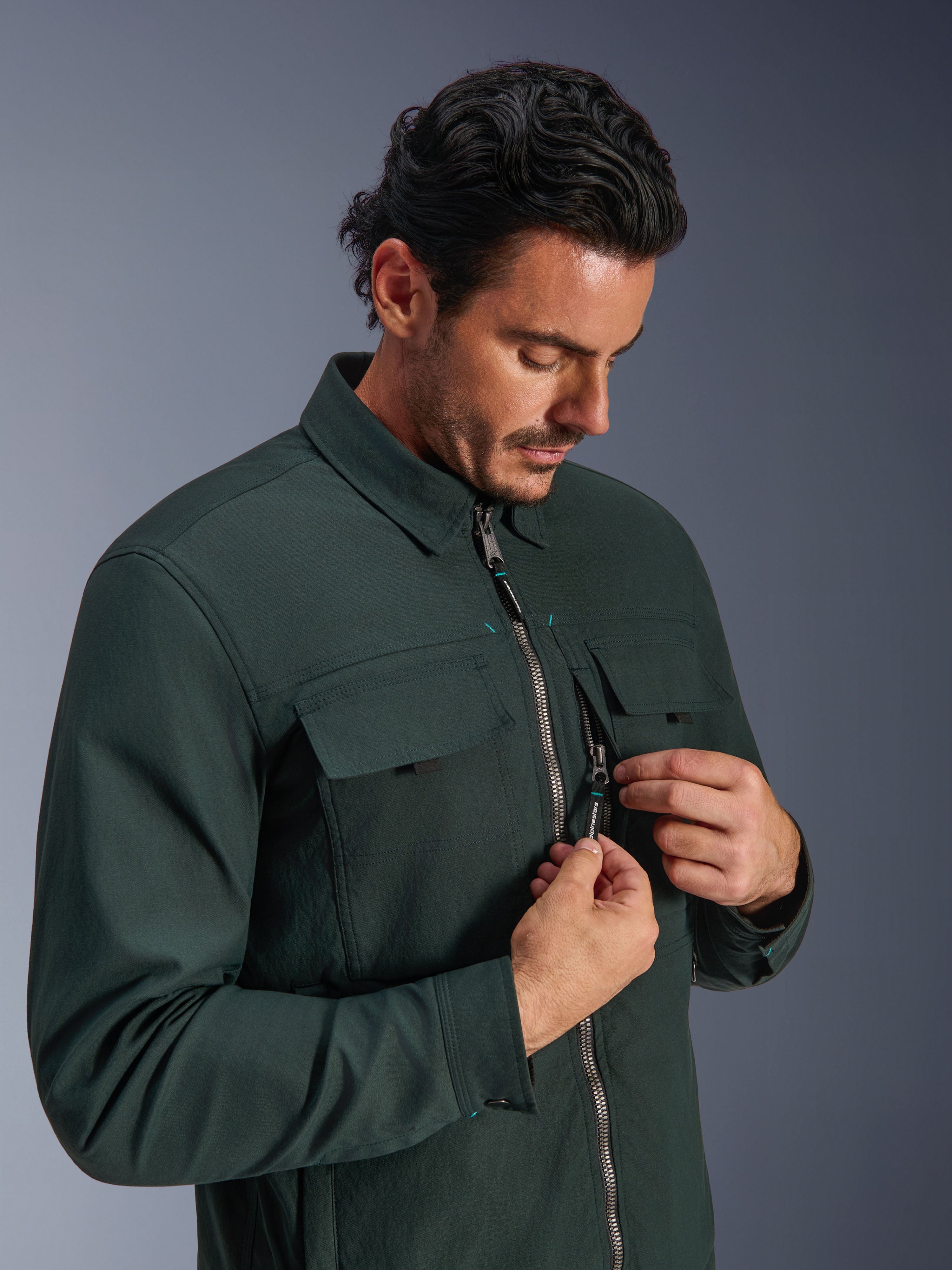 Alpinestars Bryon WR Overshirt in Dark Emerald, urban motorjas, gedragen door een man die de verticale borstzak met rits en cargozakken toont, voorzien van een duurzame gewaxte canvas textuur en een op werkkleding geïnspireerd ontwerp.