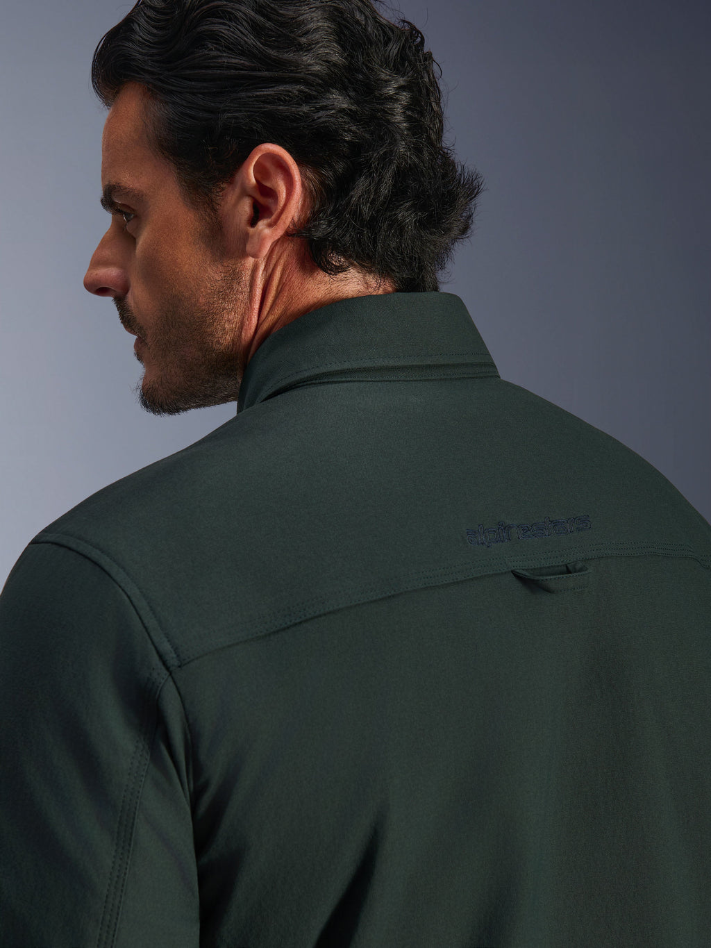 Alpinestars Bryon Water Resistant Overshirt in Dark Emerald groen, close-up van de bovenrug en kraag op een mannelijk model, voorzien van een geborduurd Alpinestars-logo en een kleine stoffen ophanglus, gemaakt van getextureerd waterbestendig gewaxt canvas voor urban motorrijden.