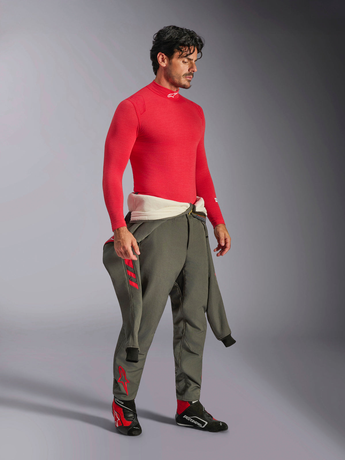 Alpinestars ZX Evo V3 Top met lange mouwen in het rood, vlamvertragende base layer voor autoracen, gedragen met olijfgroene racebroek en zwart-rode raceschoenen, professionele motorsportuitrusting, studioportret