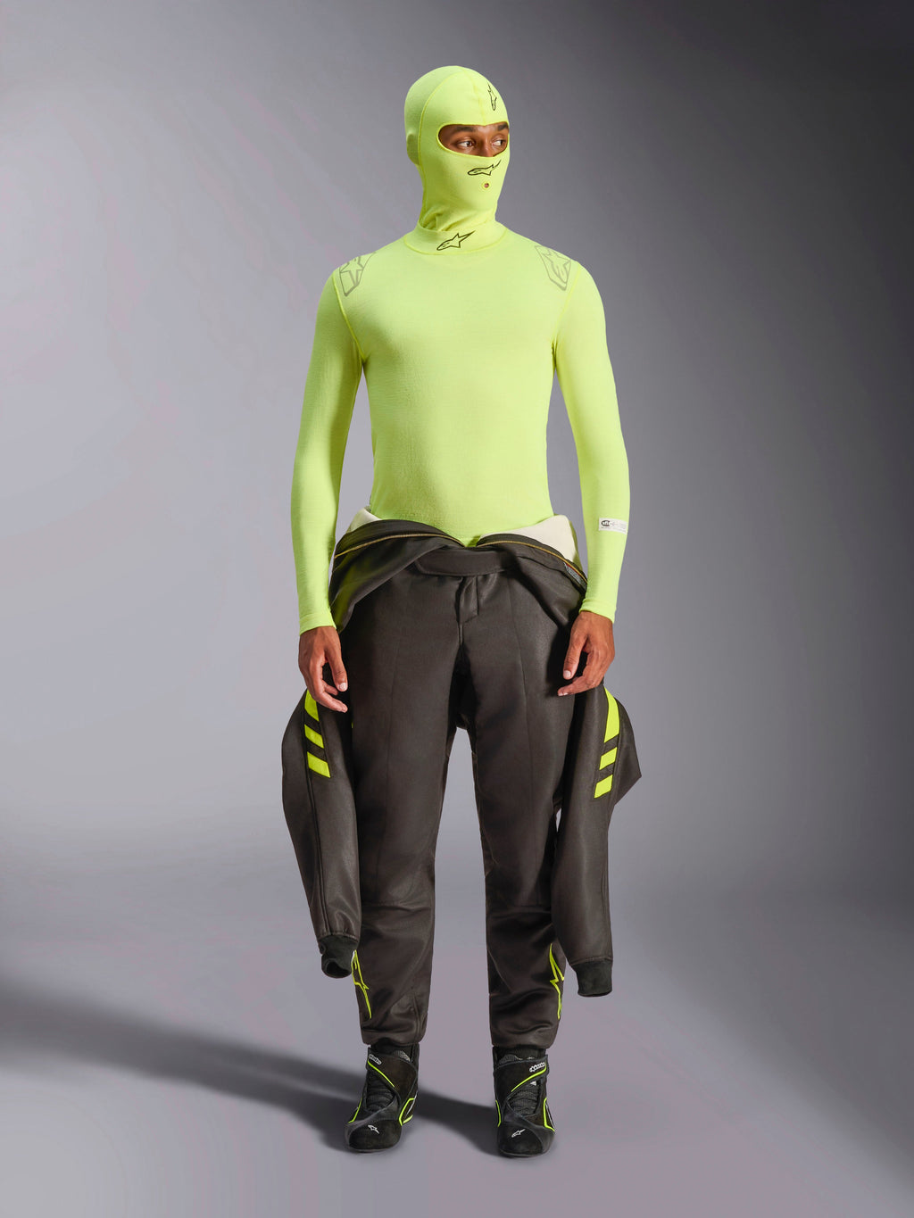 Alpinestars ZX Evo V3 Long Sleeve Top, Yellow Fluo, worn with matching balaclava and dark racing suit tied at waist, lightweight flame-resistant base layer for auto racing, featuring Alpinestars logos on the collar and shoulders