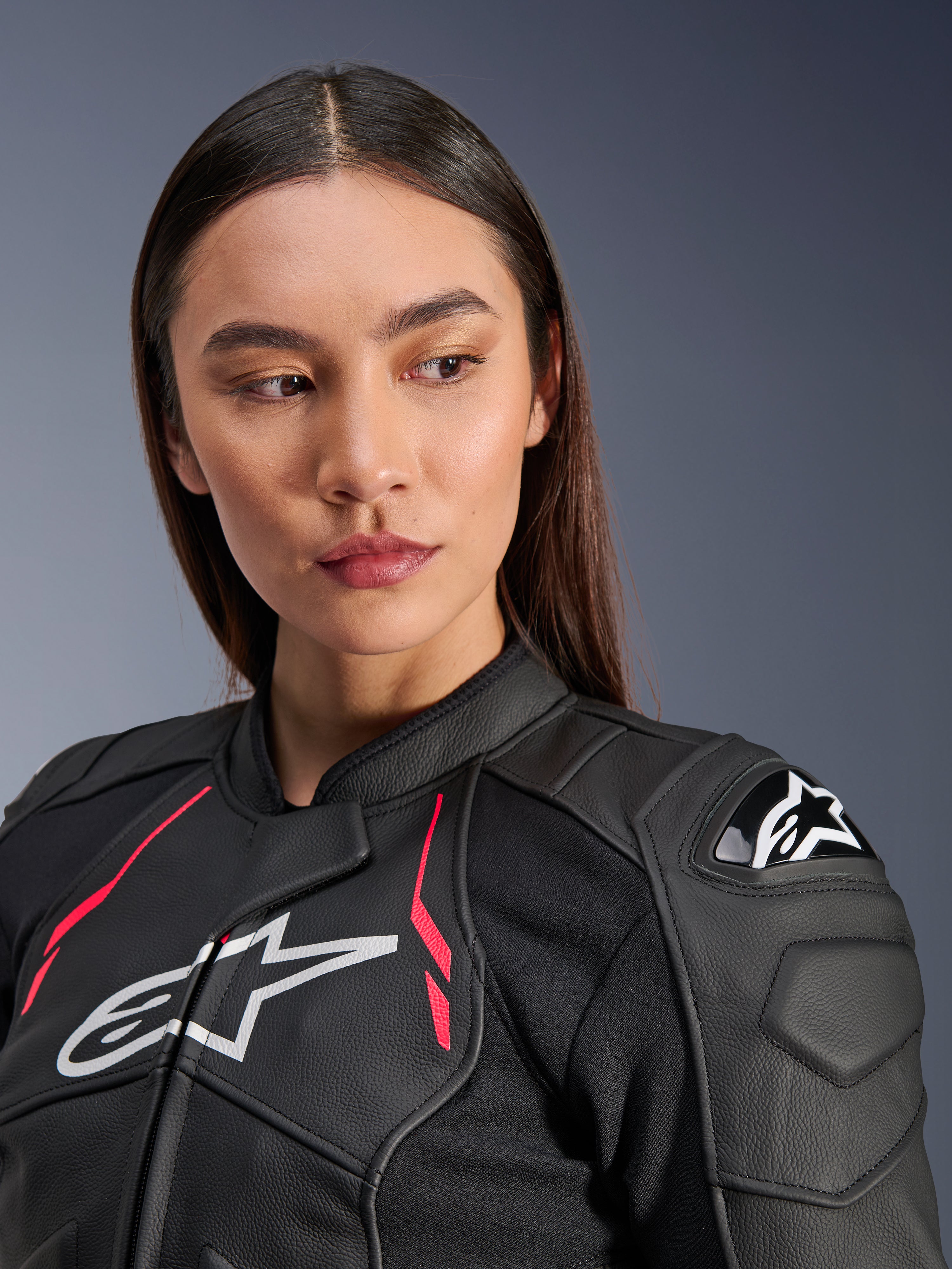 Vrouw die de Alpinestars Stella Dusk leren jas in Black Diva Pink White draagt, met een wit logo op de borst, levendige roze accenten en externe DFS-schouderbescherming, premium runderleren motoruitrusting