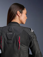 Vrouw draagt Alpinestars Stella Dusk leren jas, zwart leer met Diva Pink accenten en wit logo op de schouder, achteraanzicht met DUSK-branding en accordeon stretchpanelen, sportief ergonomisch ontwerp