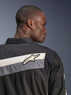 Alpinestars T-Dyno WR Jas, textiele motorjas, zwart, donkergrijs en ecru, close-up van de bovenrug en schouder met horizontale strepen en het Alpinestars sterlogo, gedragen door een model, erfgoed-geïnspireerd ontwerp voor rijden op de weg