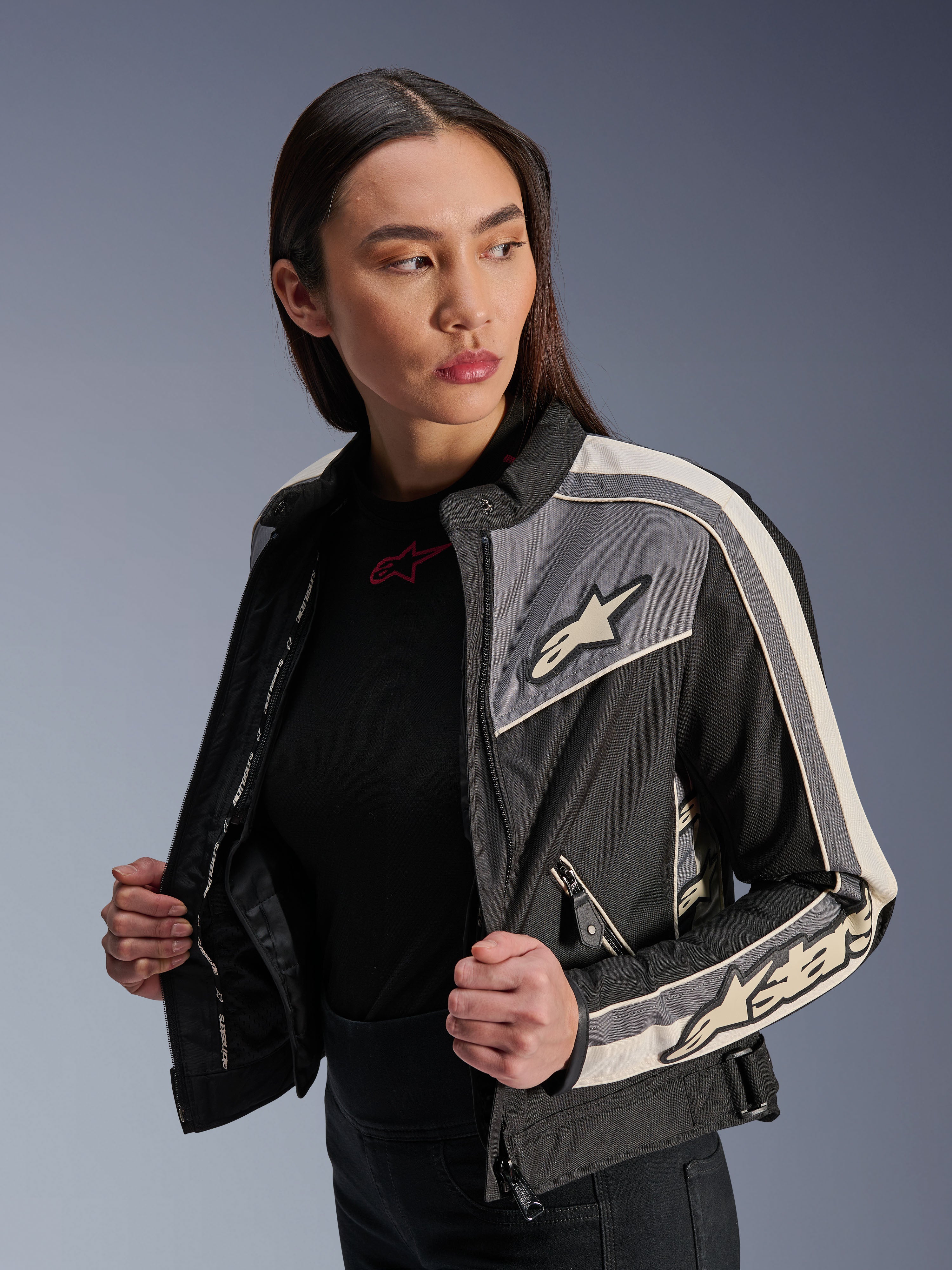 Alpinestars Stella T-Dyno WR damesjas, textiele motorjas, zwart, donkergrijs en ecru, vintage-geïnspireerd design met sportieve strepen en logo's op de borst en mouwen, gedragen door een model, urban rijuitrusting
