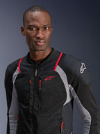 Man die het Alpinestars Troop-Air Pro Jacket draagt, zwart, asgrijs en helderrood, technische gepantserde luchtjas met ademende mesh-panelen, rode kleuraccenten en Alpinestars-logo op de schouder, urban contemporary motorkleding