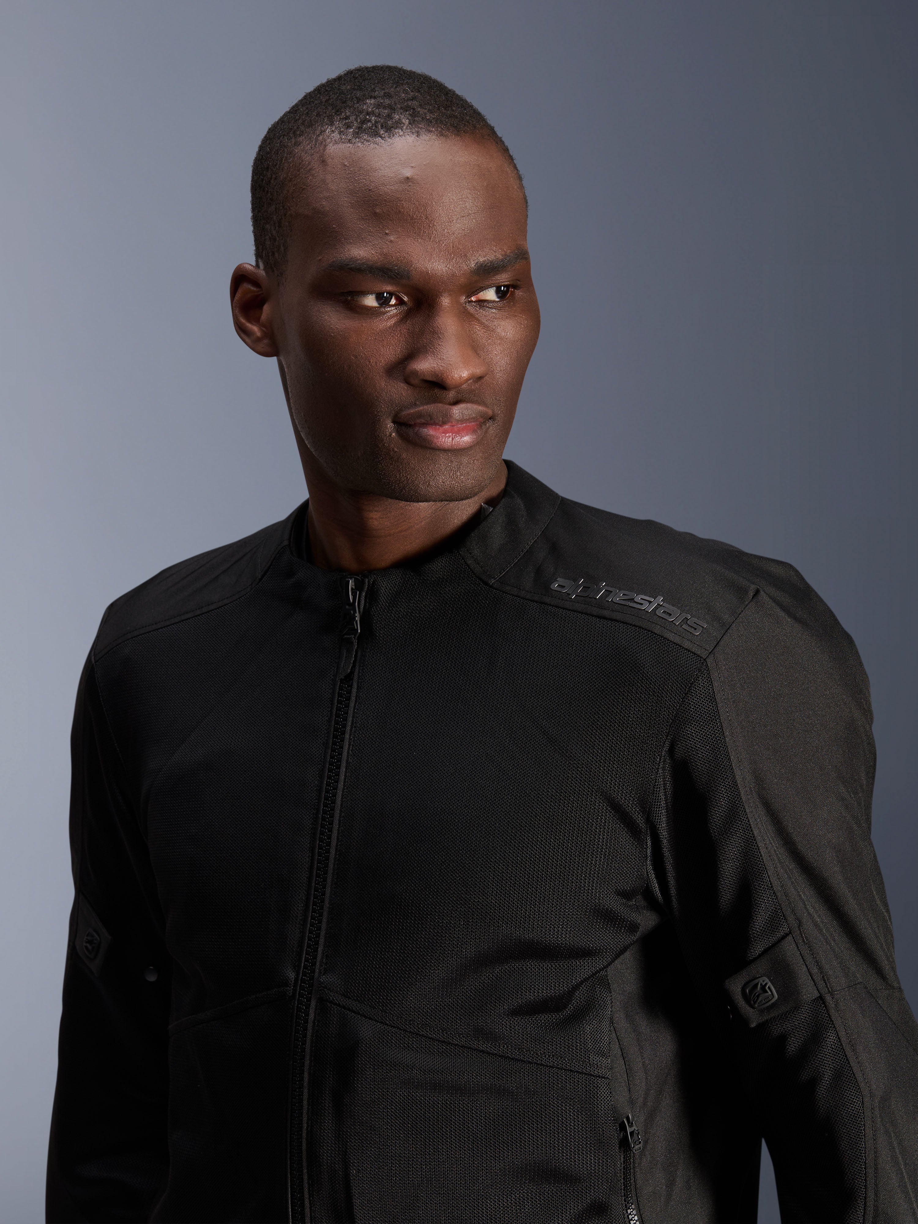 Alpinestars C-1 Air Jacket, zwarte urban motorjas met tech mesh panelen, gedragen door een model, voorzien van een subtiel hitteoverdracht Alpinestars-logo op de schouder, ontworpen voor luchtstroom en lichtgewicht comfort bij warm weer