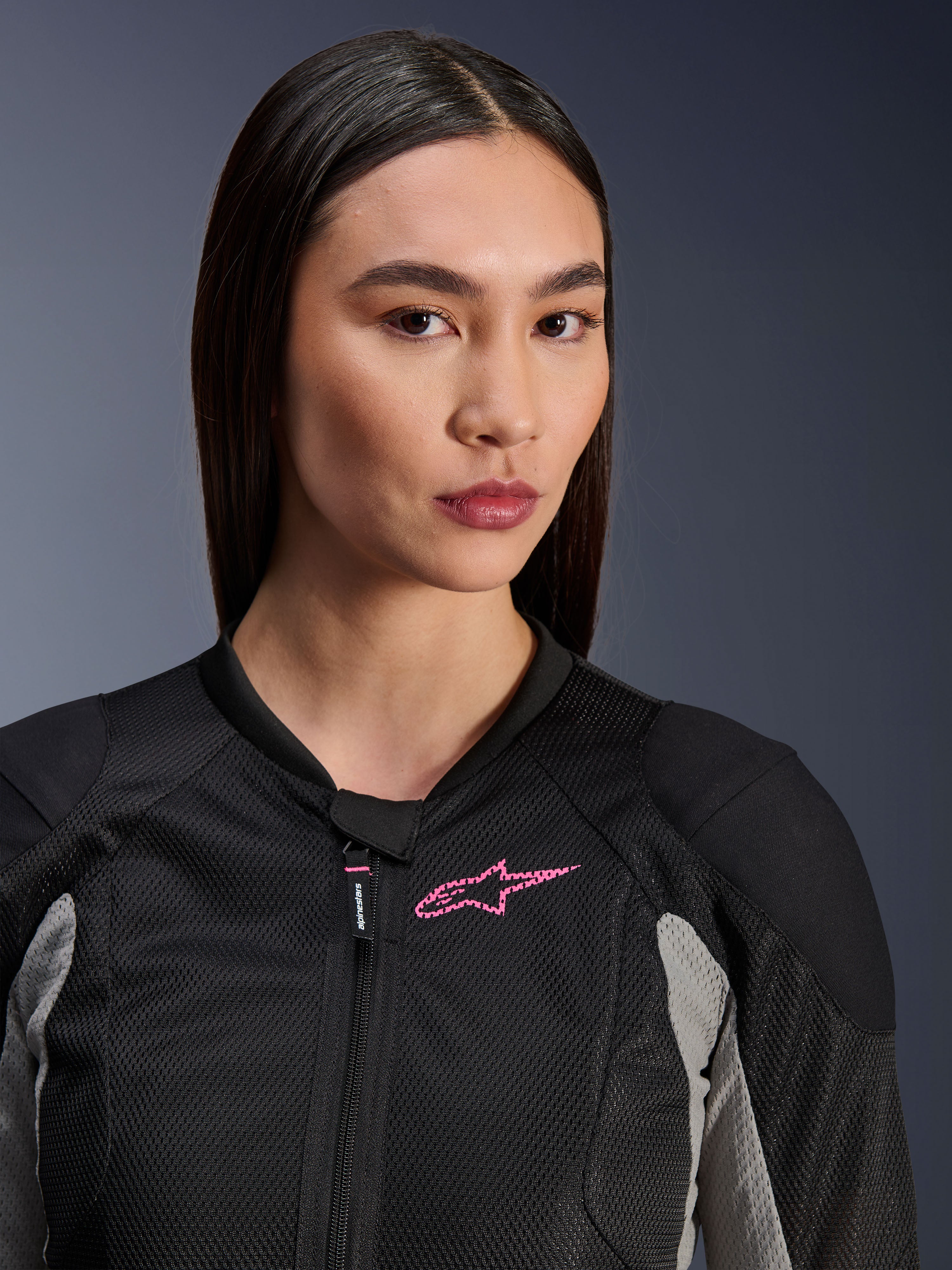 Vrouw draagt de Alpinestars Stella Troop-Air jas, Black Ash Gray en Pink Fluo, close-up weergave met nadruk op de technische mesh-constructie en het roze logo op de borst, stijlvolle urban motorkleding