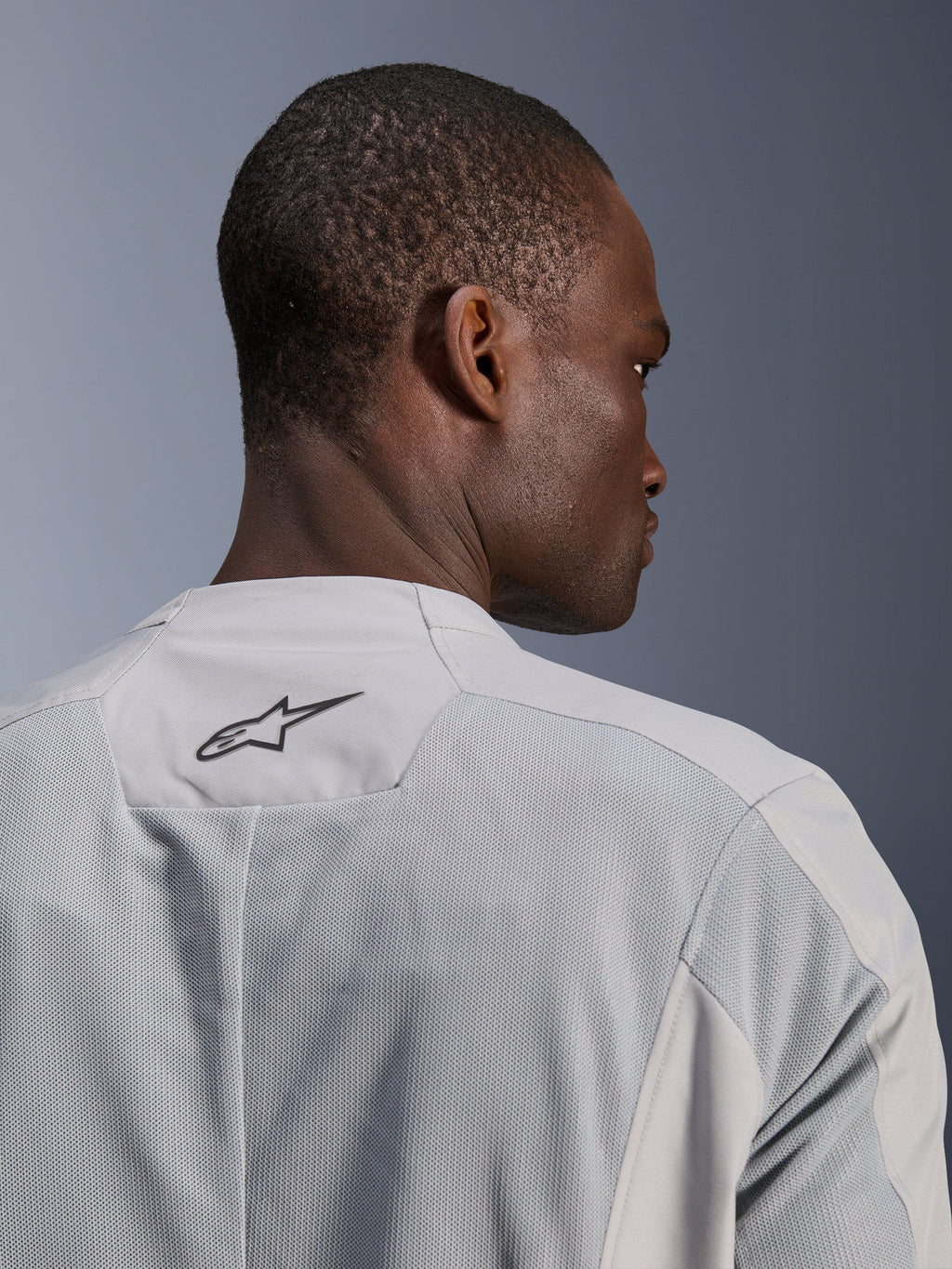 Alpinestars C-1 Air Jacket, zilvergrijze textiele motorjas, close-up van de achterkant met tech mesh-panelen voor ventilatie en een zwart Alpinestars-logo op de bovenrug, urban rider uitstraling