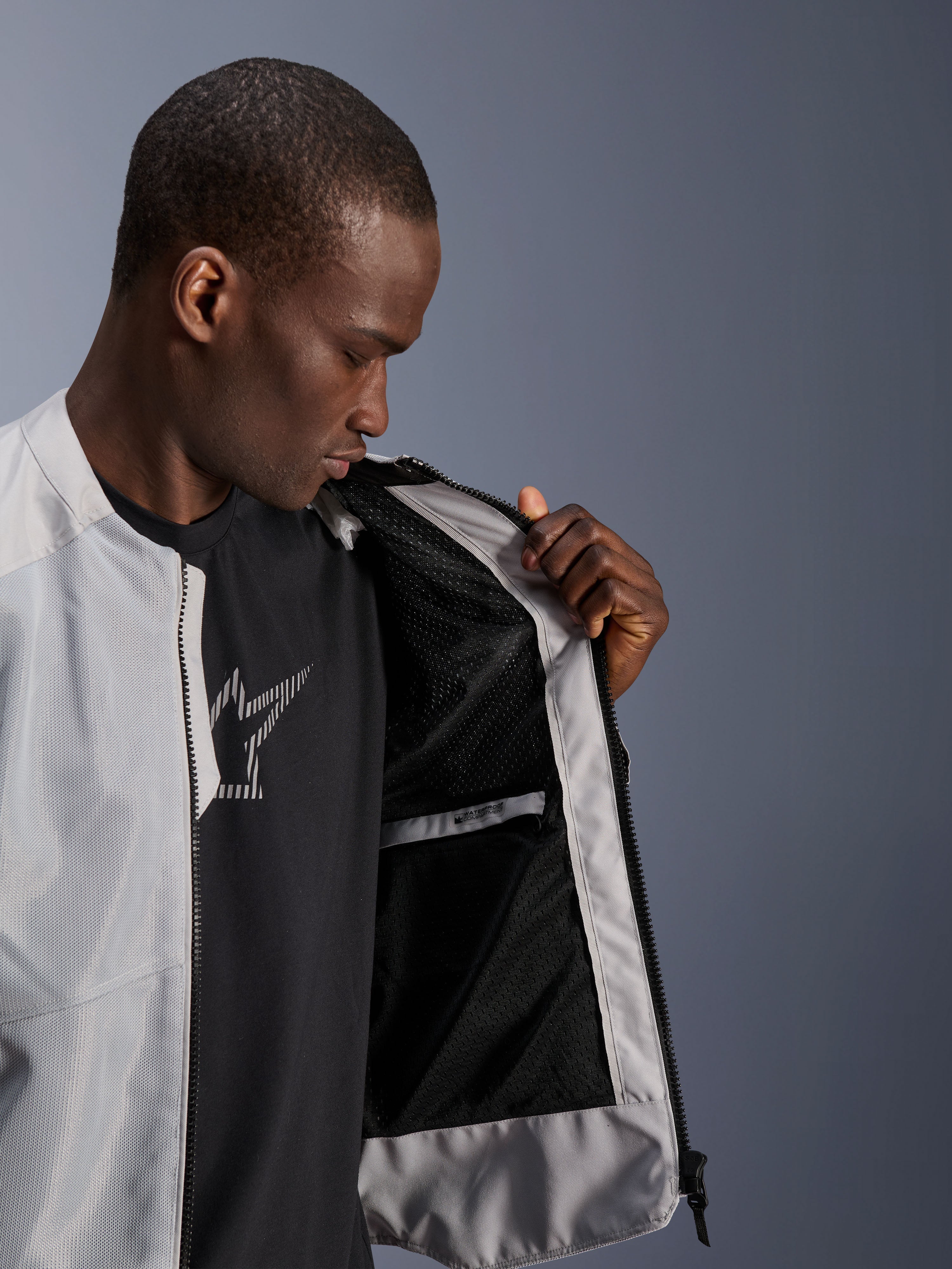 Alpinestars C-1 Air Jacket in zilver, mannelijk model opent de voorzijde van de motorjas om de zwarte tech mesh binnenvoering en waterdichte binnenzak met ritssluiting te tonen.