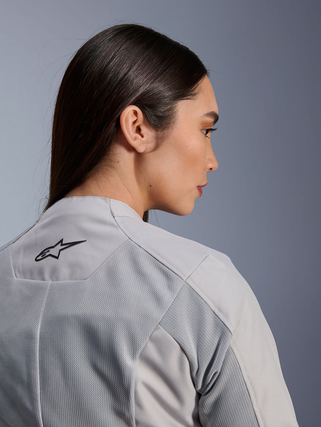 Vrouw die de Alpinestars Stella C-1 Air Jas in Silver draagt, close-up zij-achteraanzicht met het zwarte Alpinestars-logo, tech mesh ventilatiepanelen en een strak, eigentijds stedelijk motorontwerp