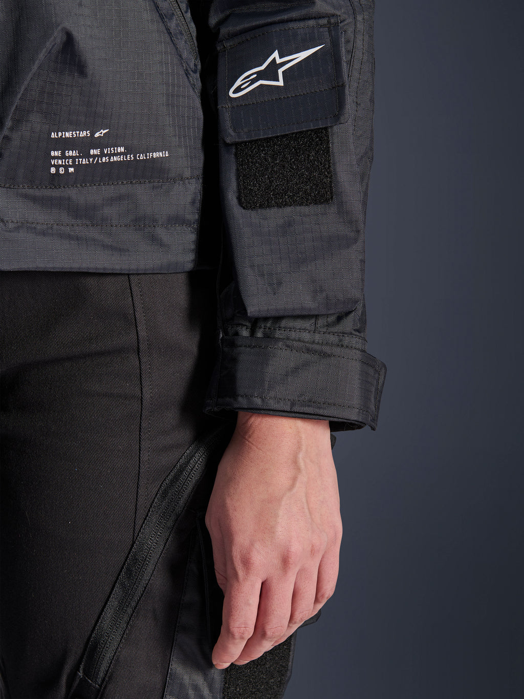 Alpinestars Molly Air jas, close-up detail van zwart ripstop-textiel, wit Astar-logo op mouwzak met klittenbandpatch, verstelbare manchet en geprinte merktekst aan de zijkant, urban motorkleding voor dames