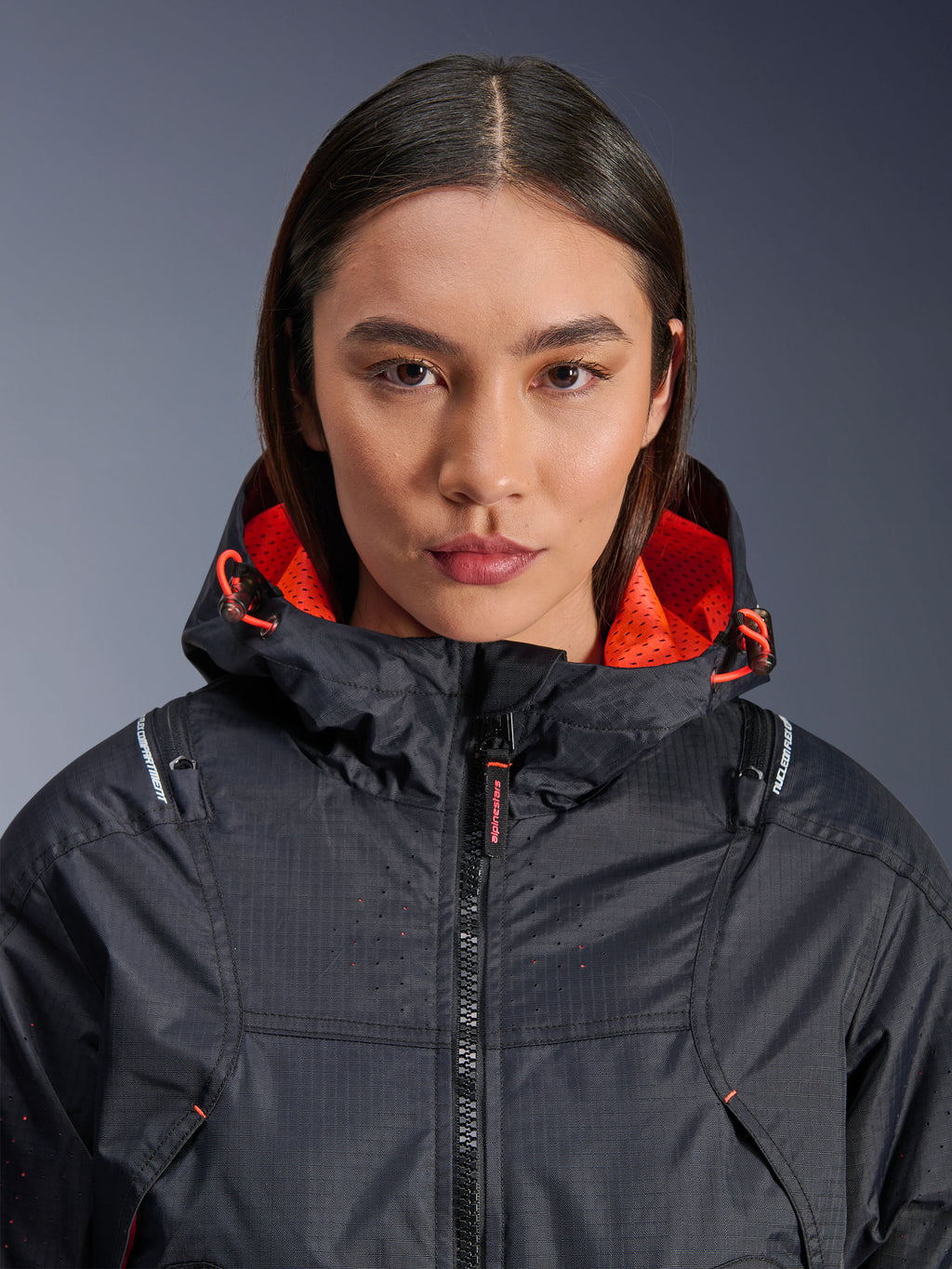 Alpinestars Molly Air Jacket, motorjas voor dames, zwart en Fluo Coral, close-up vooraanzicht op een model, ripstop textiel met laser-geperforeerde ventilatie, feloranje mesh voering in de capuchon en trekkoorden, met Nucleon Flex Plus protectie branding