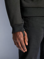 Alpinestars Chrome V2 Sport Hoodie, zwarte tech fleece, close-up van geribbelde mouwmanchet met geïntegreerde duimlus voor stabiliteit tijdens het rijden, detail van stedelijke motorkleding